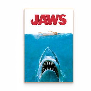 Op de afbeelding: Een rechthoekige filmposter met de rode tekst JAWS bovenaan. Onder de tekst zwemt een persoon aan het oppervlak van de blauwe oceaan. Onder water zwemt een grote haai met een open bek en scherpe tanden naar boven.