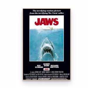 Op de afbeelding: Een filmposter voor Jaws met de titel in dikke rode letters bovenaan. Daaronder zwemt een grote haai naar een persoon die aan het wateroppervlak zwemt. De achtergrond is zwart met witte tekst met de cast en de productiegegevens.