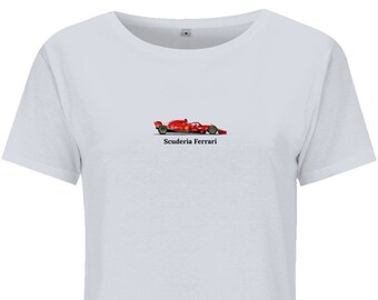 Puede incluir: Camiseta blanca con un diseño de coche de carreras Scuderia Ferrari rojo. La camiseta tiene cuello redondo y mangas cortas. El texto "Scuderia Ferrari" está impreso debajo del coche.