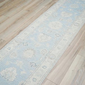 May include: A light blue runner rug with a white floral pattern. The rug is laid out on a light wood floor.