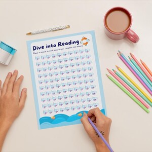 May include: A blue and white chart with the text "Dive into Reading" and a picture of a fish wearing a snorkel and flippers. The chart has 100 spaces for stickers. A hand is placing a sticker on the chart.