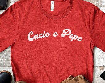 Könnte beinhalten: Rotes T-Shirt mit dem Text "Cacio e Pepe" in weißer, kursiv geschriebener Schrift.