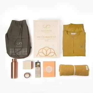 Puede incluir: Una bolsa de lona verde con cordón de ajuste con un logotipo, una botella de agua de cobre, una pequeña caja de incienso, una vela, una pequeña caja con un palo de madera en su interior, un libro con el título "The Wise Ones", una esterilla de yoga amarilla, un conjunto de pantalones y camiseta amarillos, y una caja con el texto "KOSMOI THE 7 ELEMENTS KIT MEDITATION & YOGA ESSENTIALS (सत्व)"