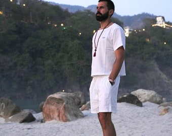 May include: A white short-sleeved top and matching white shorts set. The top features a round neckline and a small logo on the chest. The shorts have an elasticated waistband and side pockets. A beaded necklace with a tassel hangs around the neck.