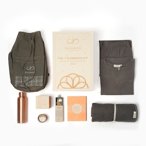 Puede incluir: Un kit de meditación y yoga con una bolsa de cordón verde, una botella de agua de cobre, una caja de incienso, una pequeña caja de madera con un amuleto dorado, un libro con el texto "We Are Enough", una esterilla de yoga gris y un conjunto de pijama gris con un logotipo blanco.