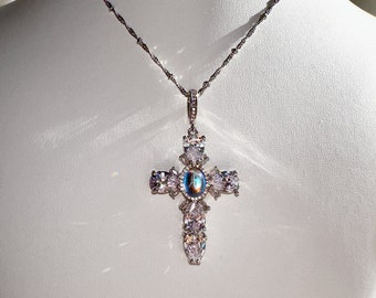 May include: A silver chain necklace with a crystal cross pendant. The cross is adorned with clear and iridescent stones.