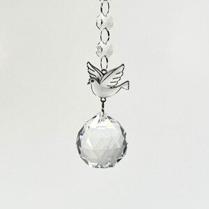 May include: A crystal prism hanging from a silver chain with a silver dove charm. The dove is in flight and has a clear crystal ball at the bottom.