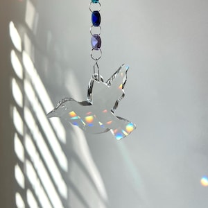 May include: A crystal dove hanging from a chain with blue and purple beads. The dove is iridescent and catches the light.