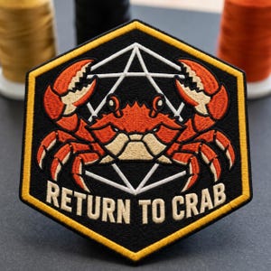 May include: A hexagonal embroidered patch with a black background and a yellow border. It features an orange crab centered over a white geometric star shape. The text "RETURN TO CRAB" is embroidered in white capital letters along the bottom edge.