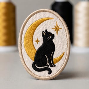May include: An oval-shaped embroidered patch featuring a black cat sitting in front of a large yellow crescent moon. The background is off-white with two gold-colored four-pointed stars. The patch has a beige stitched border around the entire edge.