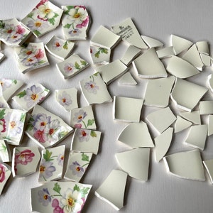 May include: A collection of broken white ceramic pieces with floral patterns. Some pieces have a pink, purple, and green floral design, while others are plain white.