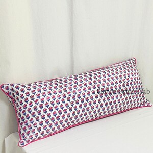 May include: Rectangular decorative pillow with a white background and a repeating floral pattern in pink and blue. The pillow has a pink border and is placed on a white surface.