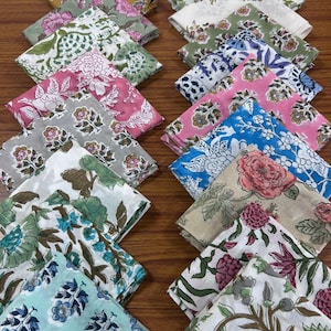 Pode incluir: Uma coleção de 16 quadrados de tecido coloridos com padrões florais. Os quadrados estão dispostos em duas filas de oito, com a fila superior ligeiramente deslocada da fila inferior. Os quadrados de tecido são todos de cores e padrões diferentes, mas todos têm um estilo semelhante. Os quadrados de tecido são feitos de um material macio de algodão e seriam perfeitos para acolchoar, fazer artesanato ou fazer roupas.