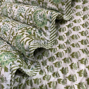 May include: A white and green floral patterned quilt. The quilt features large green floral designs and smaller green floral patterns. The edges are trimmed with a green and white striped border. The quilt is folded, showing the different patterns.