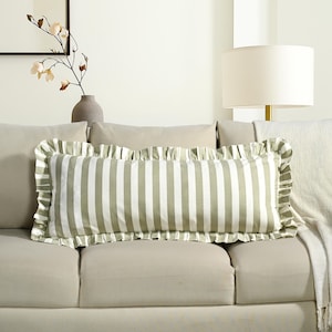 May include: A rectangular decorative pillow with a green and white striped pattern. The pillow has a ruffled edge and is placed on a beige sofa. The pillow measures approximately 20 inches long.