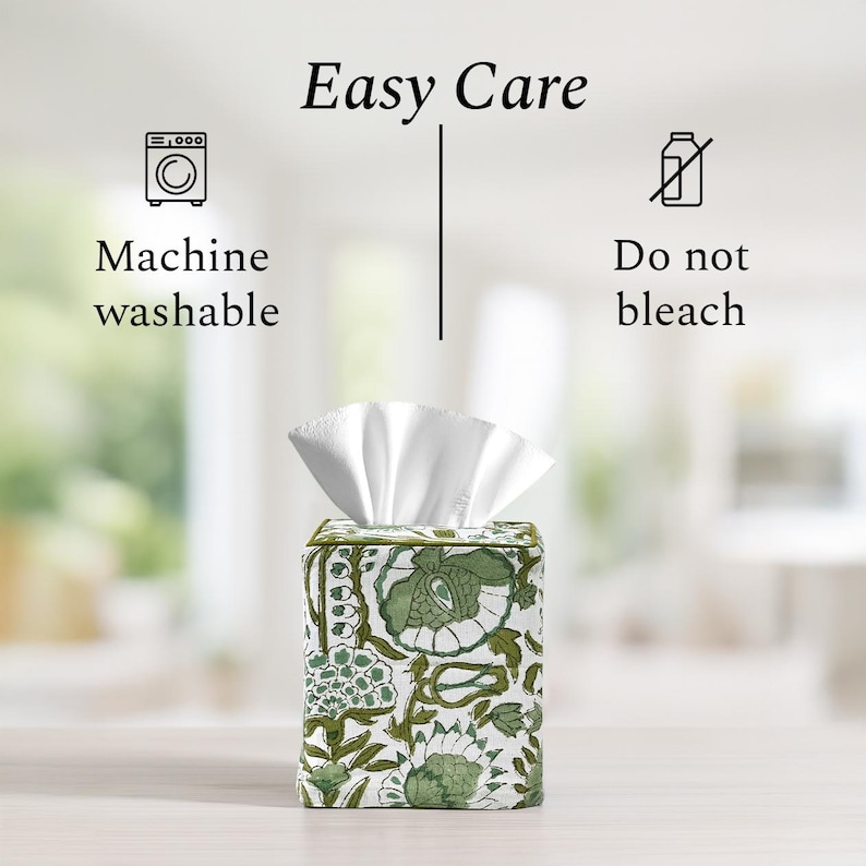Fabric tissue box cover with green floral design on a light wood surface with blurred background. Text reads: "Easy Care" with icons and instructions: "Machine washable" and "Do not bleach."