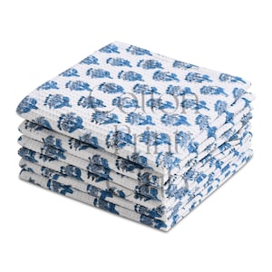 May include: A stack of white cotton washcloths with a blue floral pattern. The washcloths are folded and stacked neatly, showing the textured fabric and the repeating design. The image is well-lit, highlighting the details.