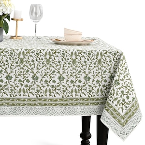 Pode incluir: Uma toalha de mesa branca com um padrão floral verde cobre uma mesa. A toalha de mesa tem uma borda com um design detalhado. Um prato, tigelas e uma taça de vinho estão sobre a mesa. Um castiçal e flores também são visíveis.