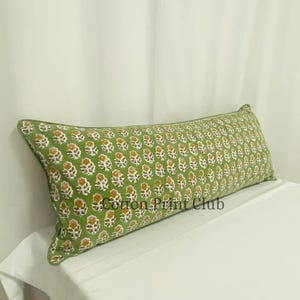 May include: A long, rectangular pillow with a green background and a repeating floral pattern in yellow and white. The pillow has a green border and the text "Cotton Print Club".