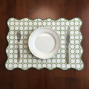 Può includere: Un piatto bianco con bordo argentato è appoggiato su un sottopiatto fantasia con bordo smerlato verde. Una forchetta e un coltello sono posizionati su entrambi i lati del piatto. Il sottopiatto ha uno sfondo bianco con un motivo floreale verde.