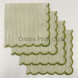 Puede incluir: Un juego de cuatro servilletas cuadradas con un patrón de rayas verticales en verde oliva y blanco. Cada servilleta tiene un borde festoneado acabado con costuras en verde oliva. El texto Cotton Print Club está centrado sobre las servilletas.