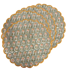 Puede incluir: Un juego de seis manteles individuales grises con un estampado floral en rosa, blanco y dorado. Cada mantel individual tiene un borde festoneado con un borde dorado. Los manteles individuales están dispuestos superpuestos.