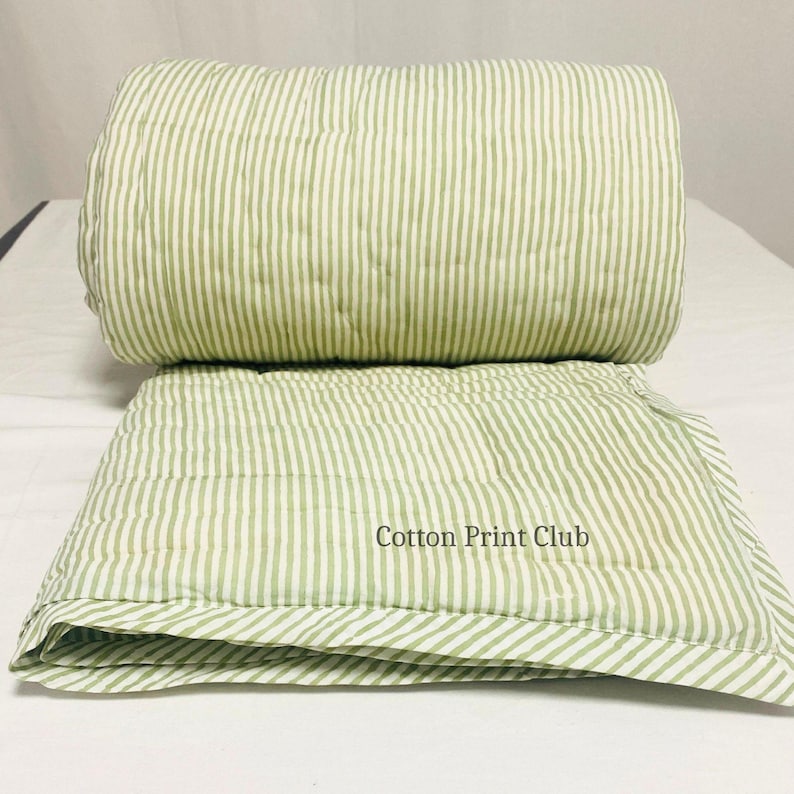 Lifestyle shot of reversible cotton Kantha quilt with stripe pattern, adding eco-friendly, artisanal charm to a cozy bedroom setup, great as throw, coverlet, or decorative bedding. Artisan-crafted green stripe quilt, fully reversible, showing hand block printed stripes on cotton, soft and durable, perfect for everyday use or gifting, farmhouse and boho décor compatible.