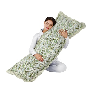 Pode incluir: Uma almofada de corpo longa e retangular com um padrão floral em tons de verde e azul sobre um fundo branco. A almofada tem uma borda com babados em verde coordenado. A almofada está sendo segurada por uma pessoa.