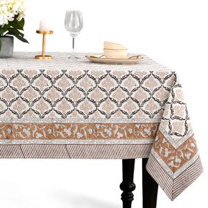 Puede incluir: Un mantel rectangular con un patrón floral marrón y negro repetido sobre un fondo blanco. El borde presenta un diseño floral marrón y rayas marrones y blancas. El mantel está sobre una mesa negra.