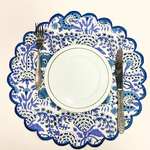 Puede incluir: Un plato blanco con borde dorado se encuentra sobre un mantel individual floral azul y blanco. Un tenedor y un cuchillo plateados se colocan a ambos lados del plato. El mantel individual tiene un borde festoneado.