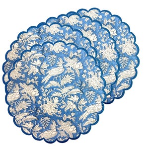 Puede incluir: Un conjunto de seis manteles individuales azules con borde festoneado. Cada mantel individual presenta un patrón floral y de pájaros blanco. Los manteles individuales están dispuestos en forma de abanico, mostrando el diseño detallado y el contraste de color.