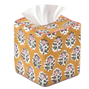Puede incluir: Una funda cuadrada para caja de pañuelos con un estampado floral amarillo mostaza. El diseño presenta flores rosas y grises con hojas verdes sobre un fondo blanco. Los bordes están ribeteados con un fino borde rosa. Los pañuelos blancos son visibles en la parte superior.