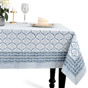 Puede incluir: Un mantel blanco y azul estampado con un diseño floral. El mantel tiene un borde con un patrón de rayas. La mesa está puesta con una copa de vino, platos y cuencos.