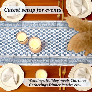 Top-down view of a beautifully arranged table with a blue and white floral table runner, cream-colored plates, white napkins, and golden cutlery. Lit candles and soft beige pampas grass add a cozy touch. Text overlay promotes the setup as the “Cutest setup for events” like weddings, holiday meals, Christmas gatherings, and dinner parties.