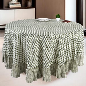 May include: A round tablecloth featuring a white base with a repeating green floral pattern. The edge of the tablecloth is finished with a gathered ruffle trim that displays a vertical green and white striped design throughout the border.