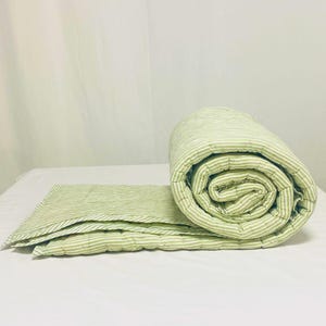 Close-up of cotton quilt texture and stitching, highlighting high-quality hand block printing, classic green stripe design, and boho-farmhouse aesthetic for bedroom décor inspiration. Green stripe quilt layered on bed, showing both sides, soft and comfortable, handmade from cotton with kantha stitching, perfect for King or Queen bed, farmhouse, or boho bedroom.