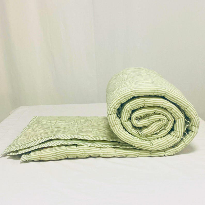 Close-up of cotton quilt texture and stitching, highlighting high-quality hand block printing, classic green stripe design, and boho-farmhouse aesthetic for bedroom décor inspiration. Green stripe quilt layered on bed, showing both sides, soft and comfortable, handmade from cotton with kantha stitching, perfect for King or Queen bed, farmhouse, or boho bedroom.