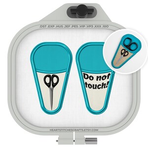 May include: Two teal and cream-colored scissor cases with black scissors. One case has the text "Do not touch!" in black. The cases are inside a gray embroidery hoop.