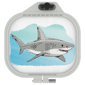 May include: An embroidered design of a white shark swimming in blue water. The design is in a white embroidery hoop with a grey plastic top. The text "DST. EXP. HUS. JEF. PES. VIP. VP3. XXX. 100" is printed on the hoop.