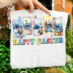 Puede incluir: Sudadera blanca con un gráfico colorido de personajes de Stitch celebrando la Pascua. El diseño incluye el texto "HAPPY EASTER" en una fuente lúdica, junto con huevos de Pascua y detalles florales. El tema general es festivo y alegre.