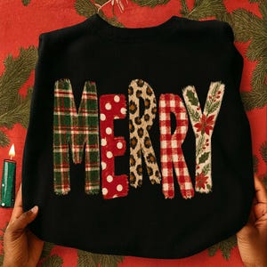 May include: A black crewneck sweatshirt featuring the word MERRY printed across the front. Each letter has a distinct pattern: the M is green plaid, the E is red with white polka dots, the R is leopard print, the R is red gingham, and the Y is floral.