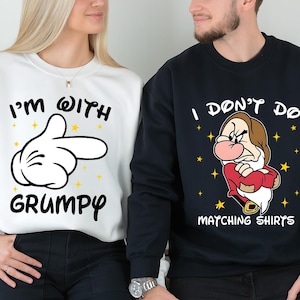 May include: Matching white and navy blue sweatshirts. The white sweatshirt features the text "I'M WITH GRUMPY" and a pointing hand graphic. The navy blue sweatshirt has a cartoon character and the text "I DON'T DO MATCHING SHIRTS".