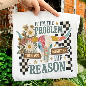 May include: White sweatshirt with a colorful floral and steer skull graphic. The text reads "IF I'M THE PROBLEM THEN YOU MIGHT BE THE REASON". The design includes flowers, stars, and a checkered pattern.