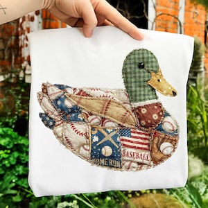 May include: White sweatshirt with a patchwork duck design. The duck has a green plaid head, a tan beak, and a body made of baseball-themed patches, including baseballs, an American flag, and the word "BASEBALL".