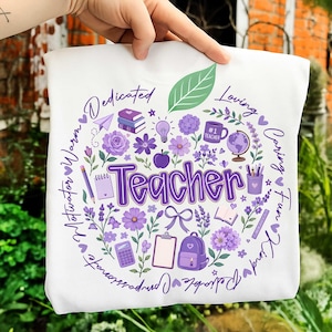 May include: White sweatshirt with a purple apple design. The design includes the word "Teacher" surrounded by flowers, school supplies, and positive words like "Loving" and "Kind".