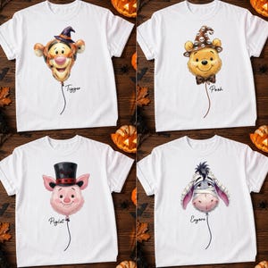 May include: Four white t-shirts featuring balloon-style illustrations of Tigger wearing a witch hat, Pooh in a skull-patterned hat, Piglet in a top hat with a bat, and Eeyore wrapped like a mummy, each with their name printed below the balloon.
