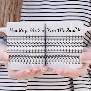 May include: Two white ceramic mugs with black text and patterns. One mug reads "You Keep Me Sane" and the other reads "Keep Me Sane" with a heart symbol. The mugs have a decorative border of geometric shapes.