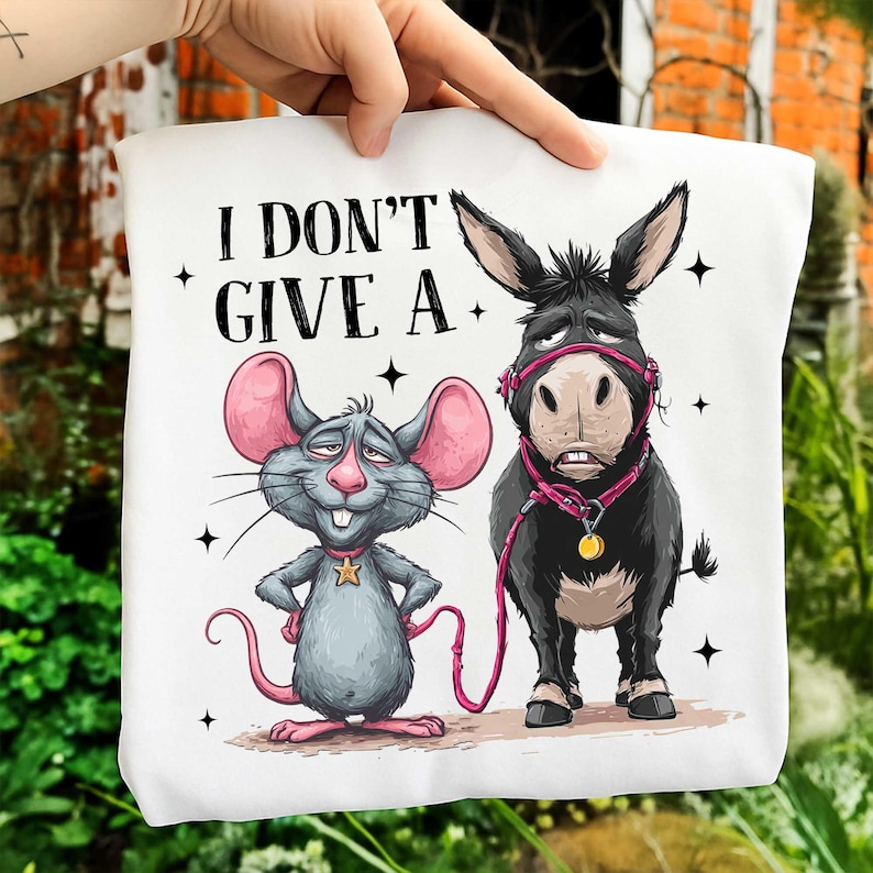 Puede incluir: Bolso tote blanco con una ilustraci&oacute;n de dibujos animados de un rat&oacute;n gris y un burro negro. El rat&oacute;n tiene orejas rosas y una cola rosa. El burro lleva un cabestro rosa. El texto "I DON'T GIVE A" est&aacute; impreso en la parte superior.