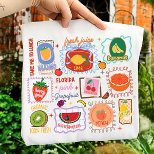 Może przedstawiać: Biała torba z kolorowymi ilustracjami owoców, takich jak mango, limonka, banany, wiśnie i arbuz. Torba zawiera napisy "Take me to lunch", "Fresh Juice", "Florida Pink Grapefruit" i "Organic 100% Fresh".