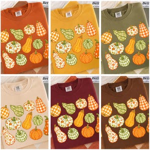 Peut inclure: Six sweat-shirts de couleur unie, ornés d'un motif répété de citrouilles et de courges illustrées en orange, vert et blanc. Les sweat-shirts sont disponibles en orange, jaune, vert olive, beige, bordeaux et marron.